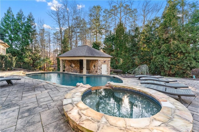 pool with a patio area, an outdoor structure, and an in ground hot tub