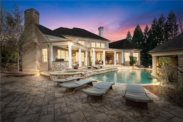 pool at dusk featuring a hot tub, an outdoor pool, a ceiling fan, and a patio