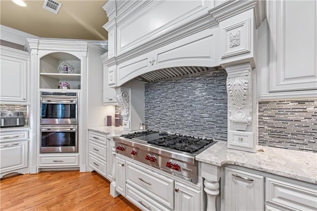 kitchen featuring visible vents, appliances with stainless steel finishes, white cabinetry, light stone countertops, and light wood-type flooring