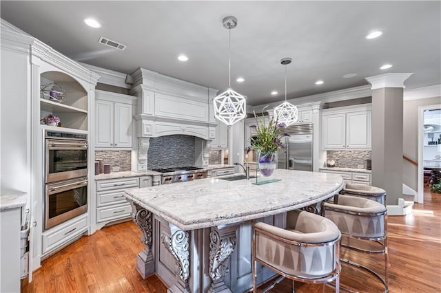 kitchen featuring visible vents, light wood-style flooring, appliances with stainless steel finishes, ornamental molding, and a kitchen island with sink