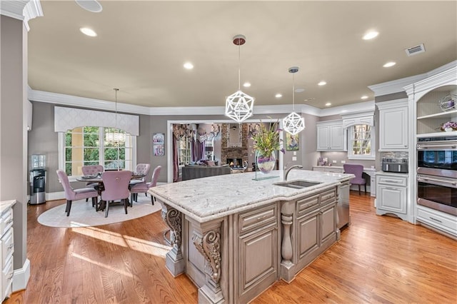 kitchen with a stone fireplace, light wood-style flooring, a sink, visible vents, and appliances with stainless steel finishes