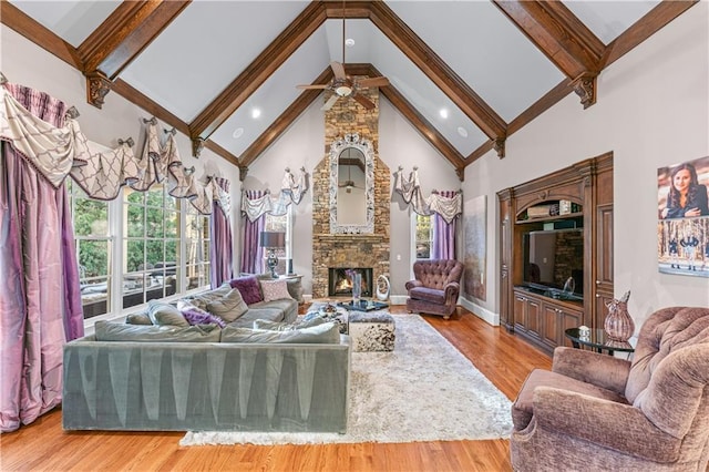 living room featuring high vaulted ceiling, a healthy amount of sunlight, a stone fireplace, and wood finished floors