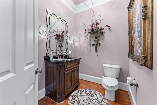 half bathroom featuring toilet, ornamental molding, vanity, wood finished floors, and baseboards