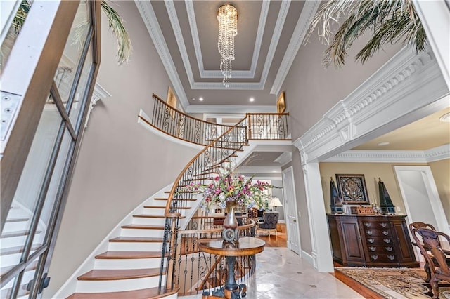 foyer with a towering ceiling, stairs, crown molding, ornate columns, and a chandelier