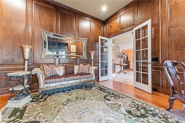 sitting room with wooden walls, visible vents, wood finished floors, french doors, and a decorative wall