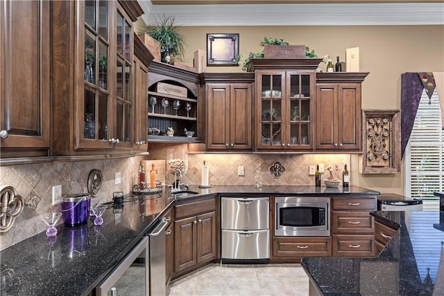 kitchen featuring stainless steel microwave, backsplash, dark stone countertops, crown molding, and a sink