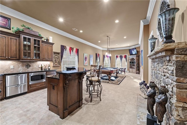 kitchen with glass insert cabinets, a breakfast bar area, stainless steel microwave, ornamental molding, and backsplash