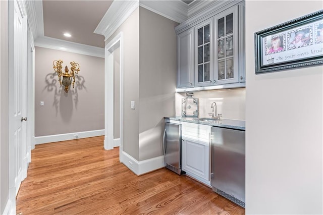 bar featuring light wood finished floors, stainless steel fridge, baseboards, ornamental molding, and a sink