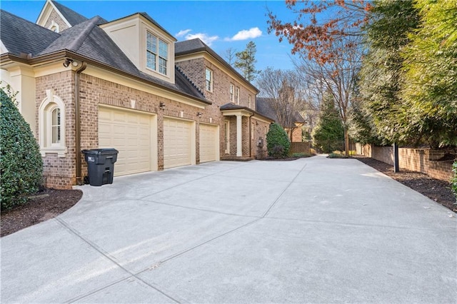 view of side of home with a garage, concrete driveway, roof with shingles, fence, and brick siding