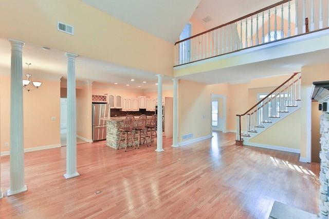 unfurnished living room with high vaulted ceiling, light hardwood / wood-style floors, and ornate columns