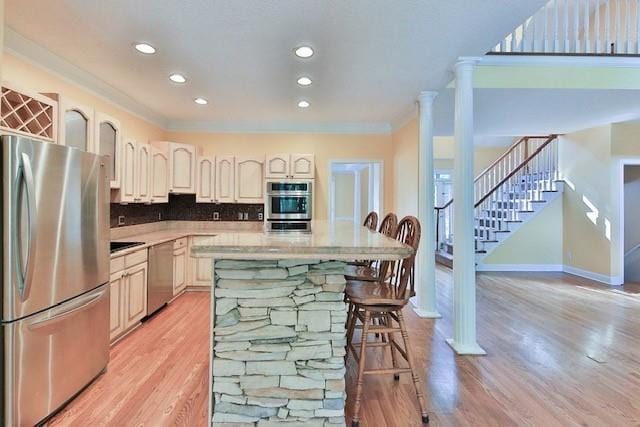 kitchen featuring tasteful backsplash, light hardwood / wood-style flooring, appliances with stainless steel finishes, a kitchen breakfast bar, and decorative columns