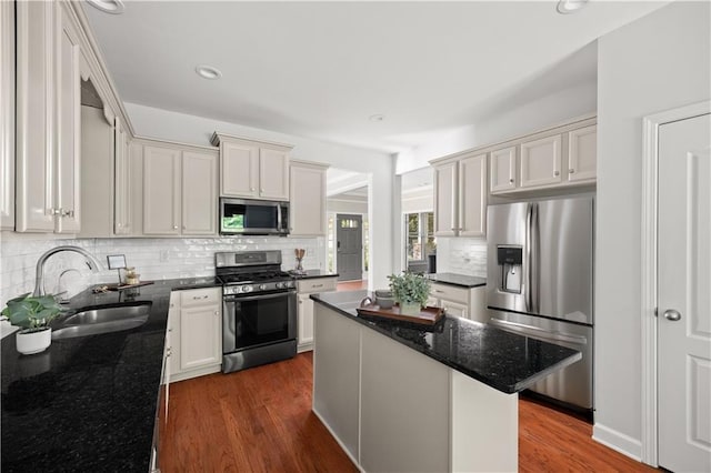 kitchen with dark stone counters, tasteful backsplash, a sink, stainless steel appliances, and dark wood-style floors