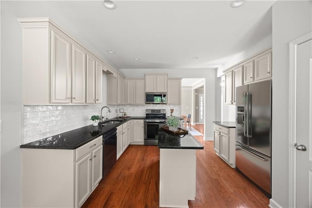 kitchen with tasteful backsplash, a sink, appliances with stainless steel finishes, a kitchen island, and dark wood finished floors