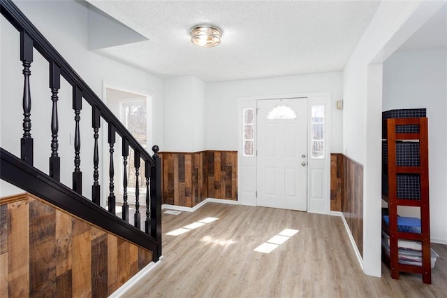 foyer featuring a textured ceiling, wooden walls, wood finished floors, stairway, and wainscoting