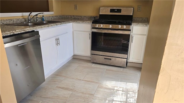 kitchen with appliances with stainless steel finishes, white cabinets, light stone countertops, and sink