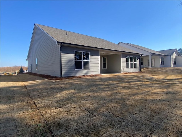 rear view of property featuring a yard and roof with shingles