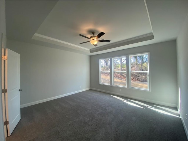 spare room with dark colored carpet, a tray ceiling, baseboards, and a ceiling fan