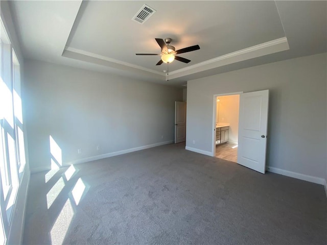 unfurnished bedroom with baseboards, a tray ceiling, multiple windows, and visible vents