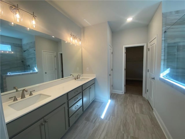 bathroom with double vanity, tiled shower, baseboards, and a sink