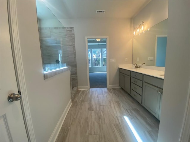 bathroom with visible vents, a walk in shower, a sink, double vanity, and baseboards