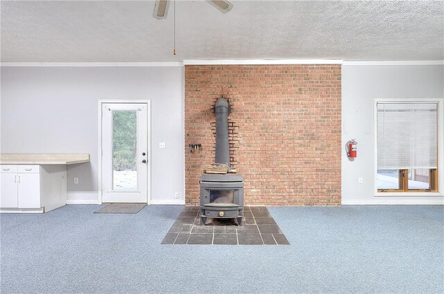 unfurnished living room with dark carpet, ceiling fan, ornamental molding, a wood stove, and a textured ceiling