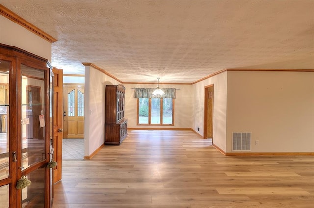 spare room with an inviting chandelier, light wood-type flooring, a textured ceiling, and ornamental molding