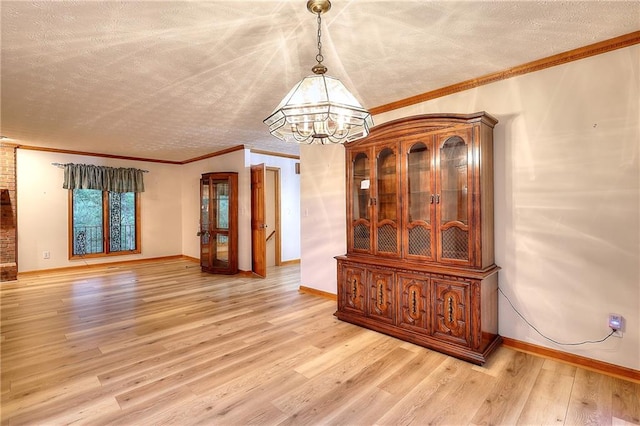 unfurnished dining area featuring light hardwood / wood-style flooring, ornamental molding, a textured ceiling, and an inviting chandelier