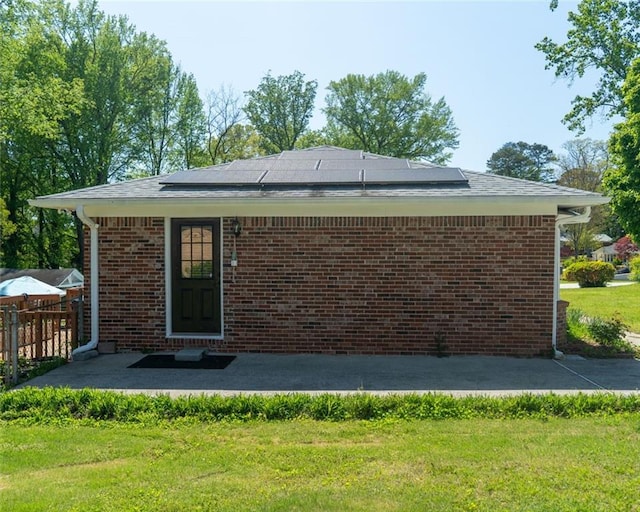 rear view of property featuring a lawn, solar panels, brick siding, and fence