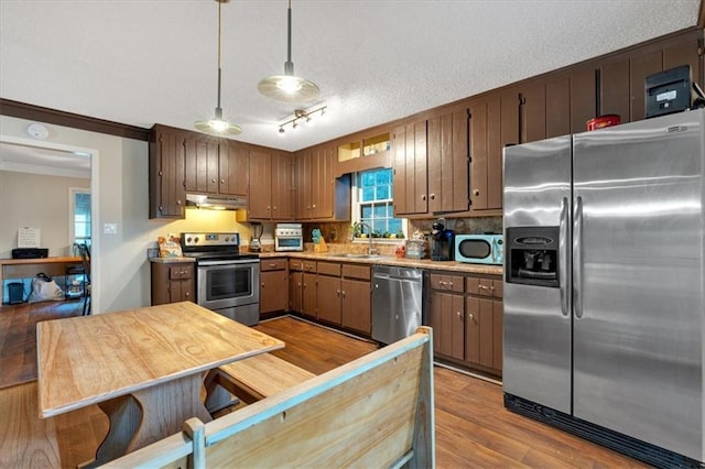 kitchen with pendant lighting, light hardwood / wood-style flooring, sink, ornamental molding, and appliances with stainless steel finishes