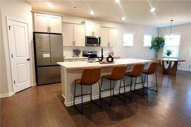 kitchen with visible vents, a center island with sink, dark wood finished floors, appliances with stainless steel finishes, and a breakfast bar area