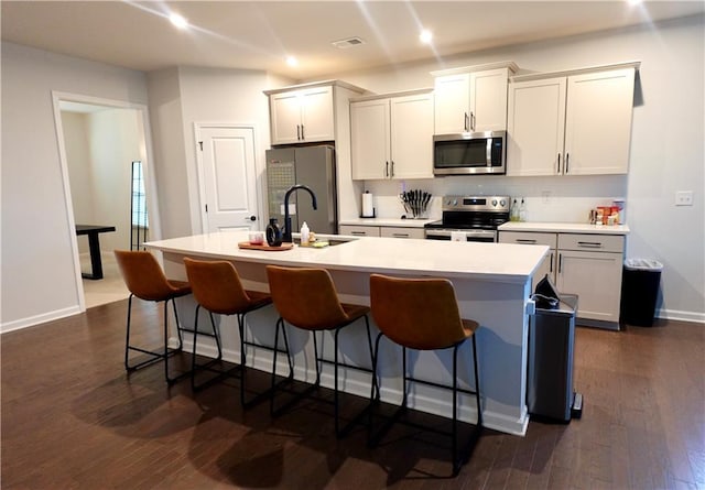 kitchen with visible vents, a center island with sink, a sink, stainless steel appliances, and a kitchen breakfast bar