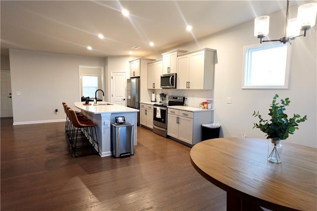 kitchen featuring a center island with sink, appliances with stainless steel finishes, a breakfast bar, and dark wood-style flooring