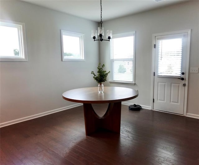 unfurnished dining area featuring dark wood-style floors, a notable chandelier, and baseboards