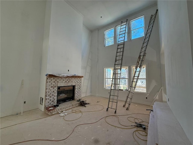 unfurnished living room featuring a brick fireplace, crown molding, plenty of natural light, and a high ceiling