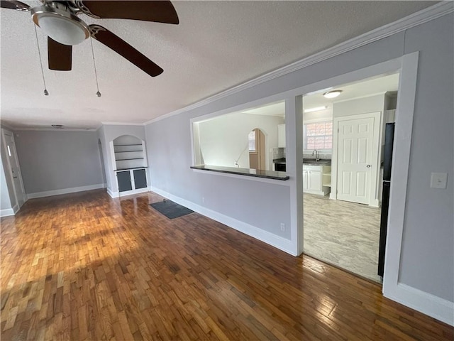 unfurnished living room with sink, crown molding, a textured ceiling, ceiling fan, and hardwood / wood-style floors