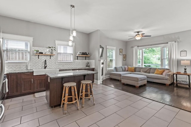 kitchen with backsplash, ceiling fan, a center island, light tile floors, and a breakfast bar