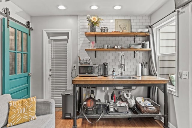 bar featuring a barn door, sink, hardwood / wood-style floors, and tasteful backsplash