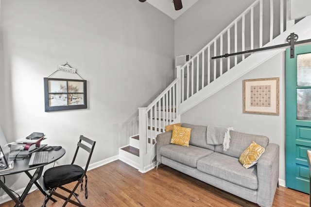 living room with a barn door, a high ceiling, ceiling fan, and hardwood / wood-style floors