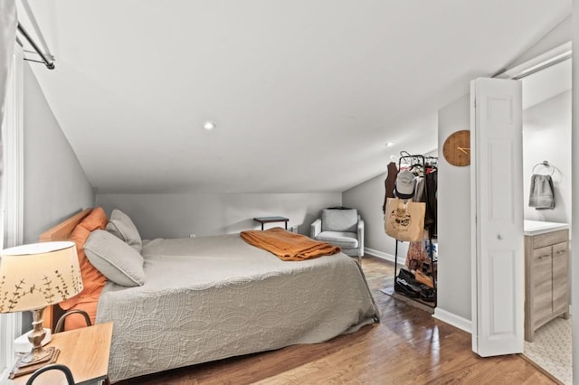 bedroom featuring vaulted ceiling, connected bathroom, and light wood-type flooring