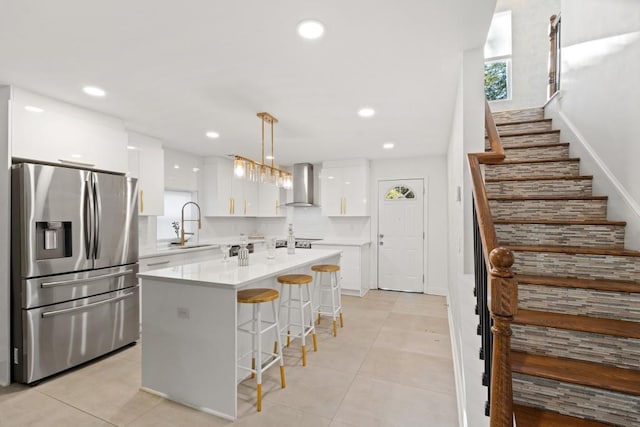 kitchen with white cabinets, a center island, stainless steel fridge with ice dispenser, wall chimney range hood, and pendant lighting