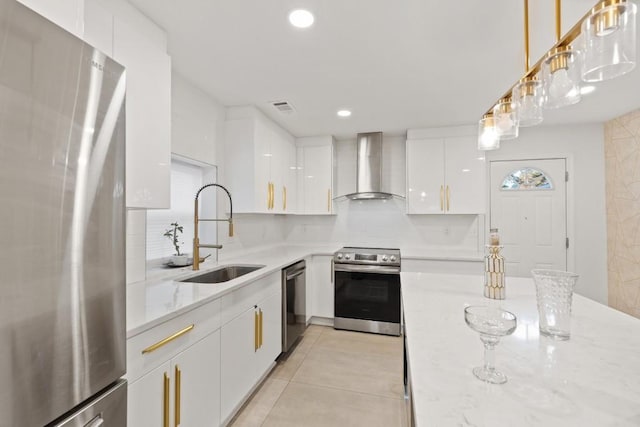 kitchen featuring white cabinets, stainless steel appliances, sink, wall chimney range hood, and decorative light fixtures