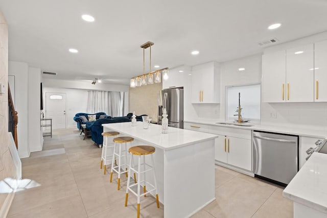 kitchen featuring appliances with stainless steel finishes, a kitchen island, white cabinets, decorative light fixtures, and light tile patterned flooring