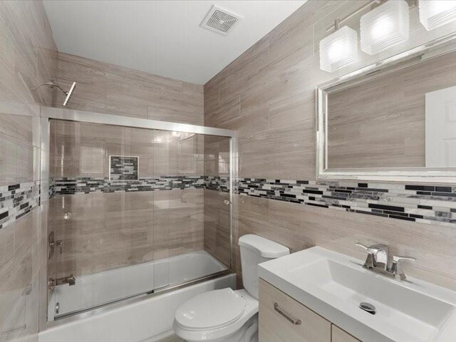 full bathroom with tasteful backsplash, tile walls, enclosed tub / shower combo, vanity, and toilet