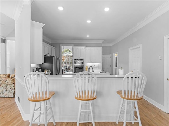 kitchen featuring a kitchen breakfast bar, stainless steel appliances, light wood-type flooring, baseboards, and a peninsula