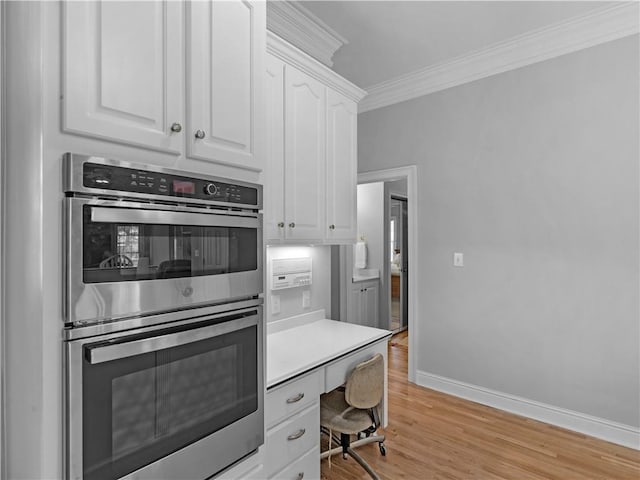 kitchen featuring double oven, light wood finished floors, crown molding, baseboards, and white cabinetry