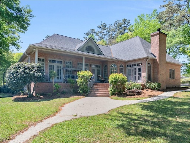 view of front of house featuring a chimney, a front lawn, roof with shingles, french doors, and brick siding