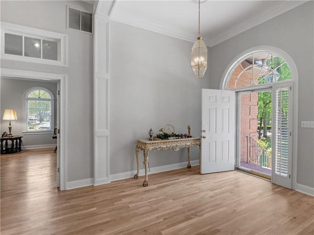foyer entrance with a notable chandelier, ornamental molding, visible vents, and light wood-style flooring