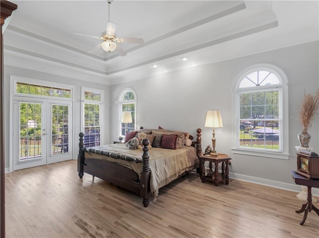 bedroom with a raised ceiling, light wood-type flooring, crown molding, and access to outside