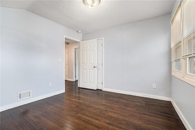 spare room featuring dark wood-style floors, a textured ceiling, visible vents, and baseboards