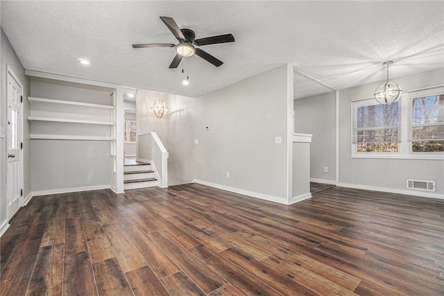 unfurnished living room with a textured ceiling, ceiling fan with notable chandelier, visible vents, stairs, and dark wood finished floors